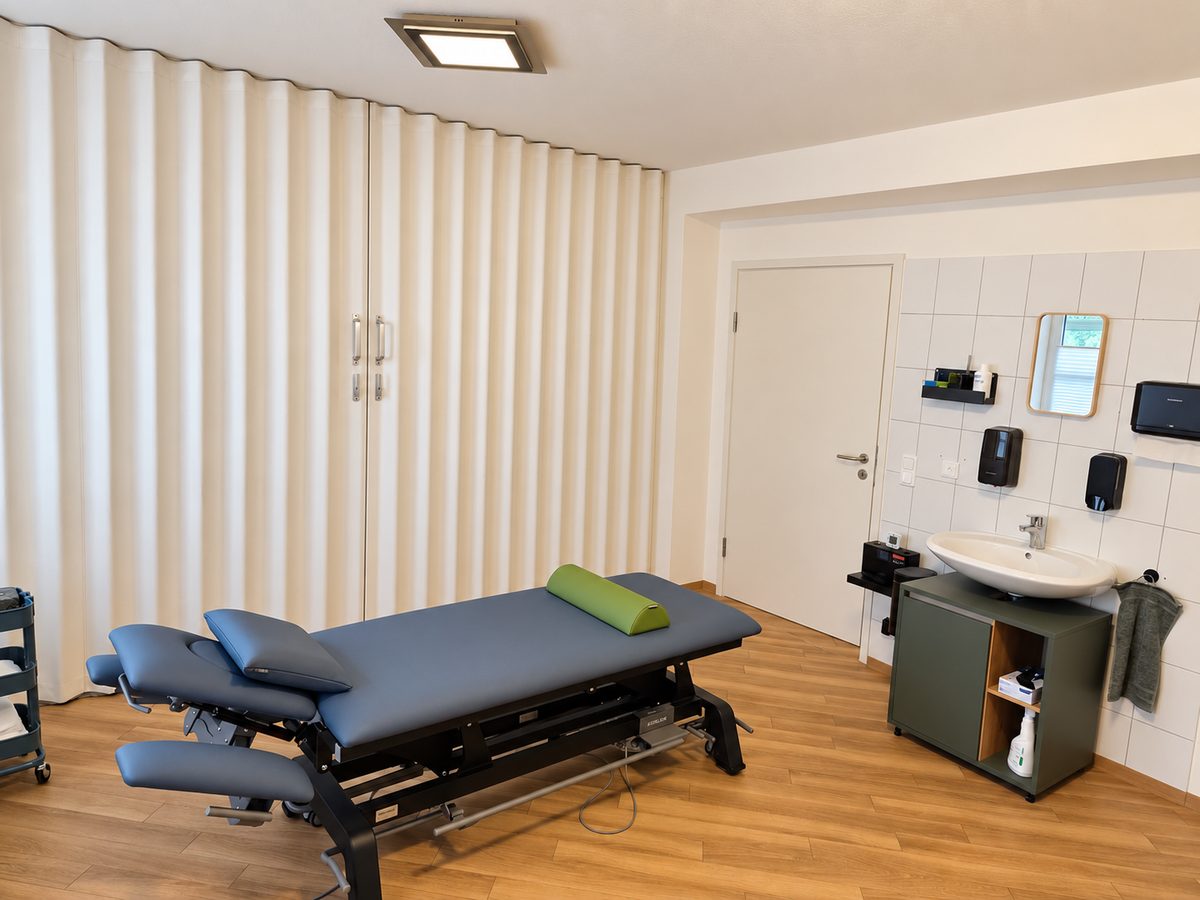 Heller Behandlungsraum mit Therapieliege und Waschbecken
